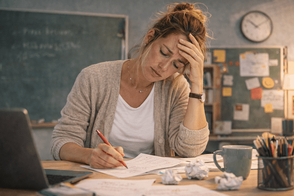 Geschenk für Lehrer – die sinnvollste Geschenkidee, die wirklich gut tut 2 Lehrkraft sitzt am Schreibtisch, korrigiert Unterlagen und wirkt erschöpft – ein realistischer Blick auf den anspruchsvollen Lehreralltag