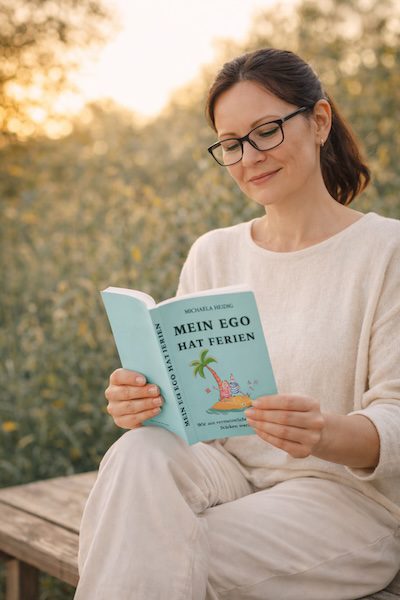 Lehrkraft sitzt draußen auf einer Bank und liest das Buch ‚Mein Ego hat Ferien‘ – ruhige Natur, Symbol für Selbstführung und Soft Skills.