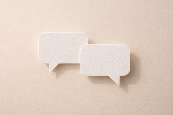 Zwei Papier‑Sprechblasen – minimalistisches Symbol für Kommunikation und Dialog.